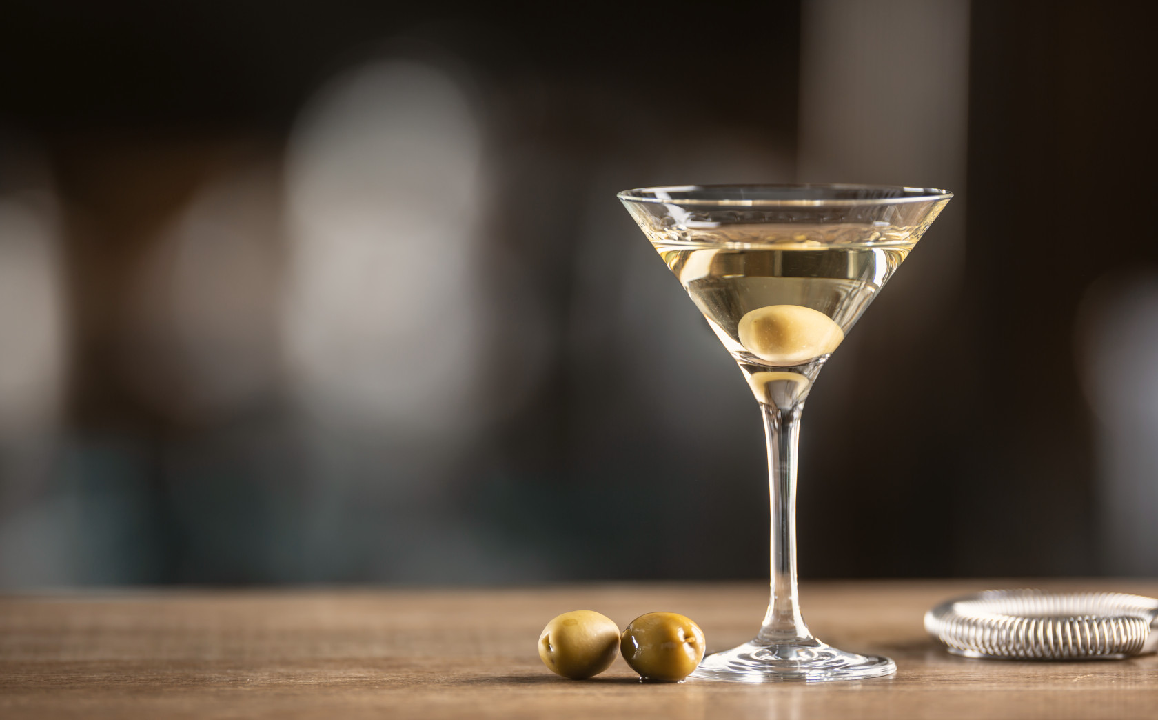 Martini sitting on a wooden bar next to two olives