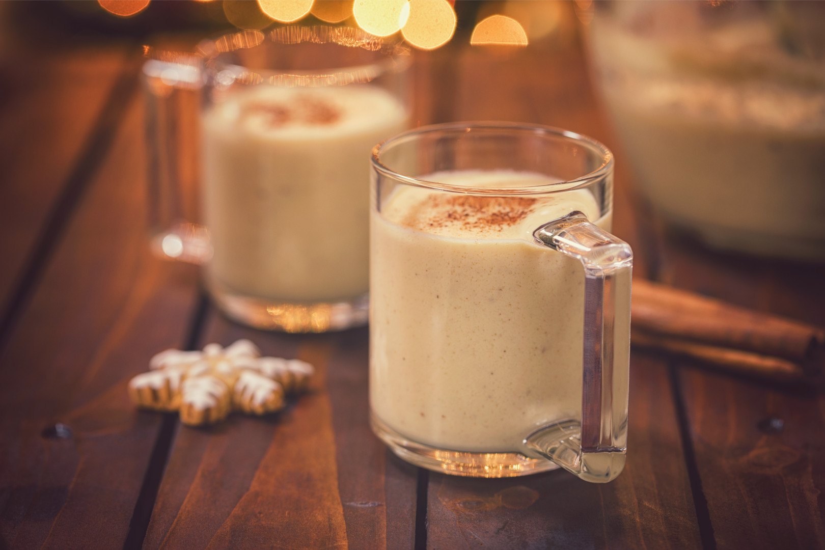 Two mugs of eggnog sitting on a wooden surface