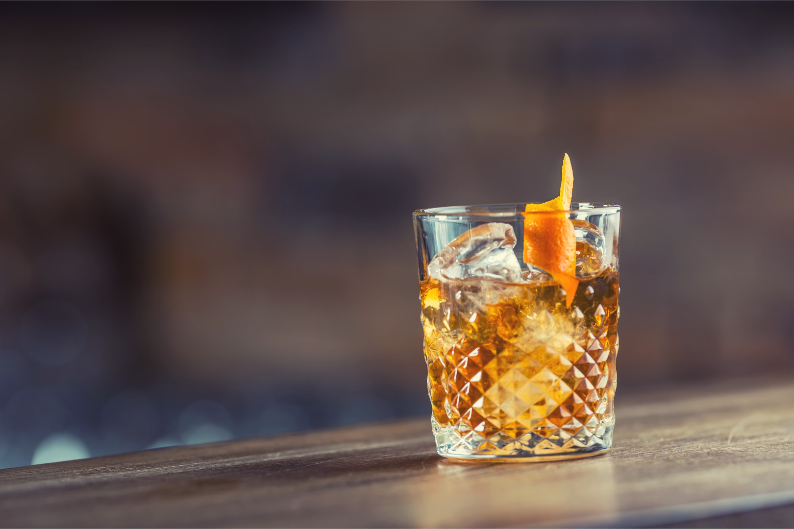 An old-fashioned with twisted orange peel sitting on a wooden bar