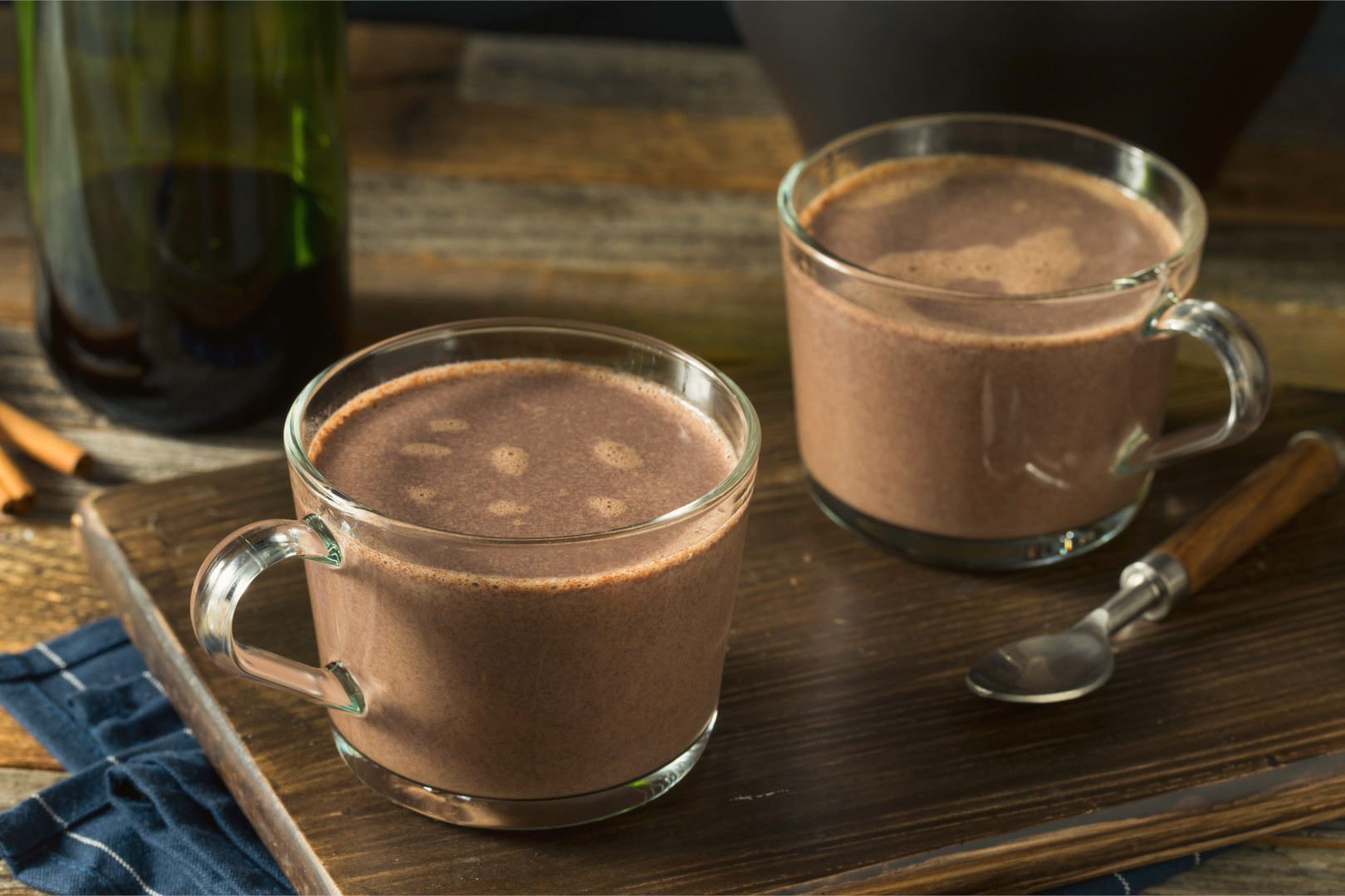 Two glass mugs of hot chocolate sitting on a wooden board