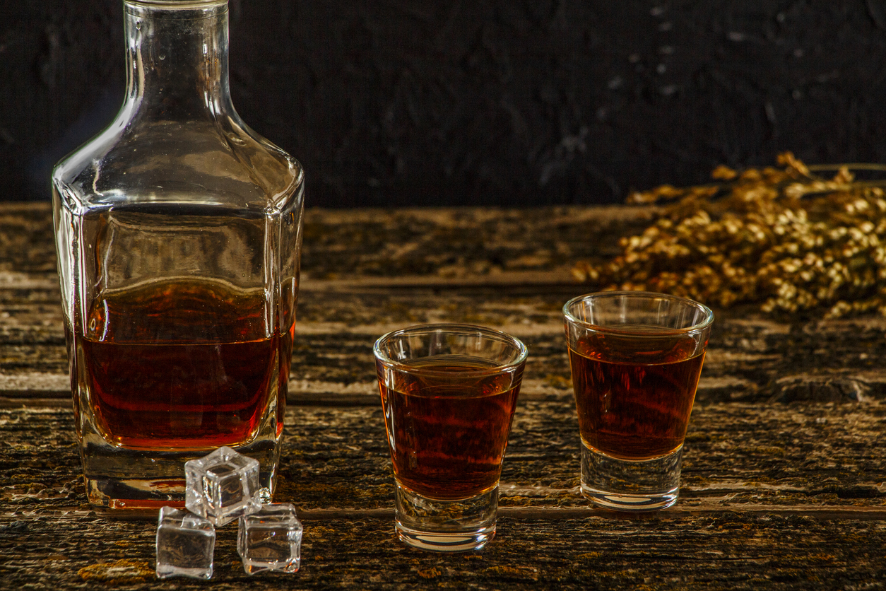 Whiskey bottle,  two shots, and ice cubes sitting on an old wooden background