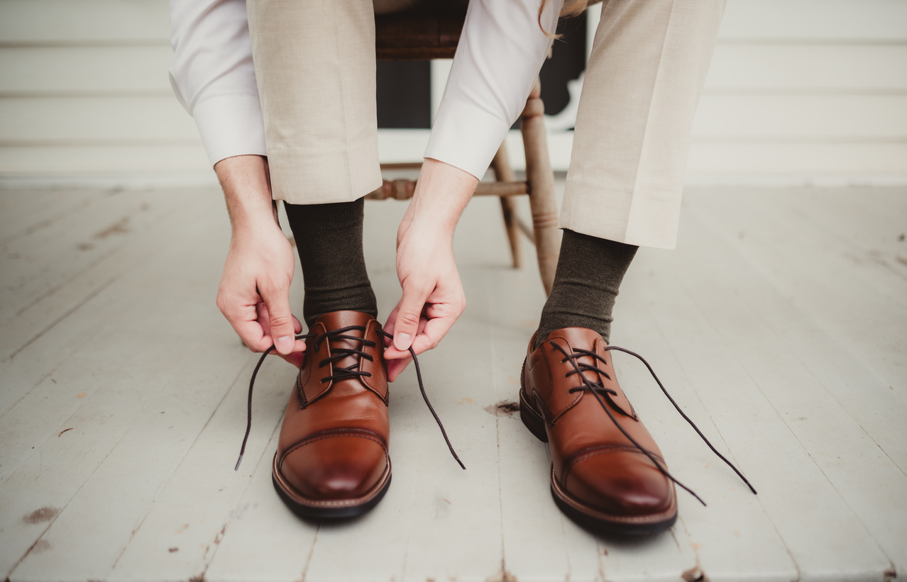 Man sitting in a chair lacing a pair of brown cap toe oxfords
