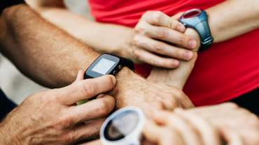 A close up of a group of amateur athletes synchronizing their smart watches together before setting off on their weekly run in the city